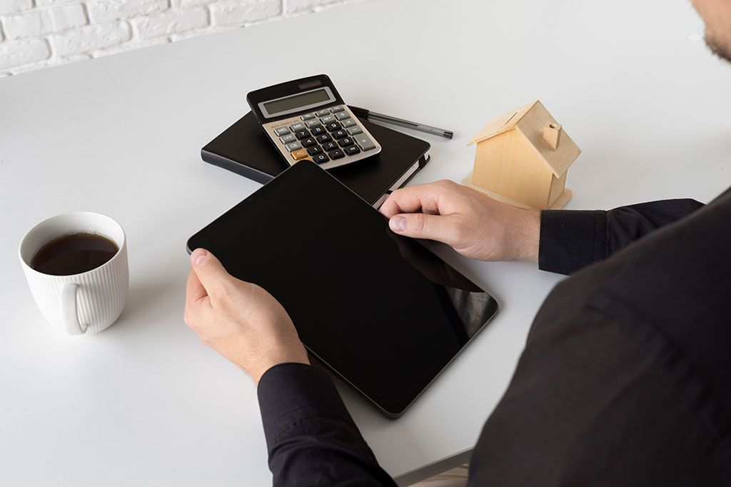 Руки держат планшет над столом, где лежат блокнот и калькулятор